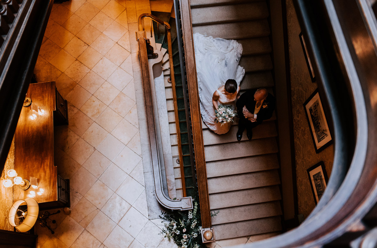 A bride walks down the staircase of the beautiful palladian house in Oxfordshire on her wedding day