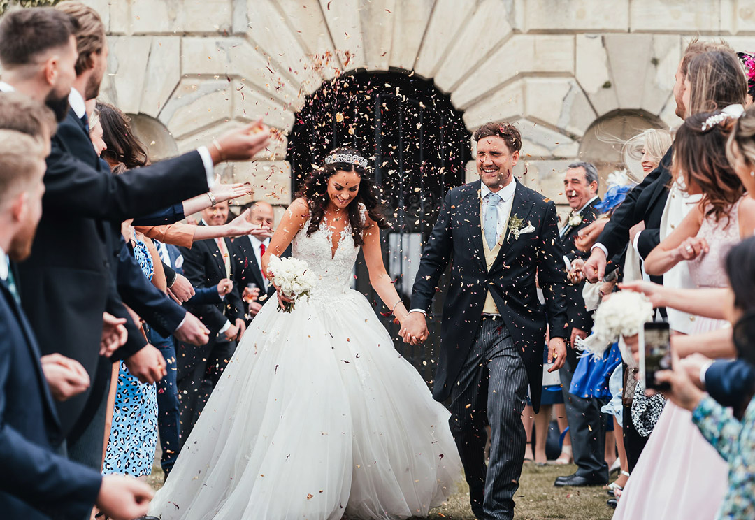 Bride and groom celebrate with friends and family within the landscaped grounds of their wedding venue, with a Palladian house as their backdrop